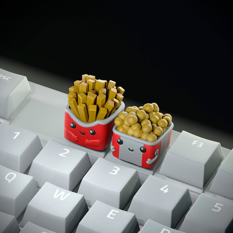 May include: Two small, cartoon-like containers with smiling faces. One container is red and holds french fries. The other container is gray and holds small, round, yellow objects. The containers are sitting on a keyboard with white keys.