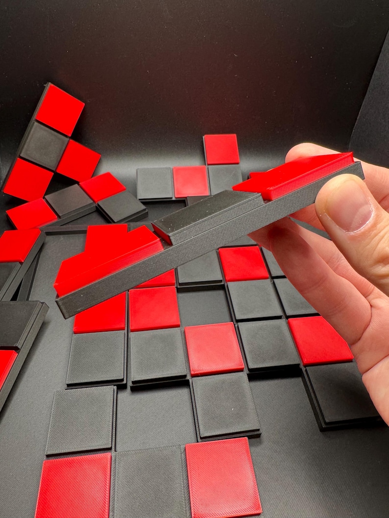 K&ouml;nnte beinhalten: Eine Sammlung roter und schwarzer geometrischer Puzzleteile. Die Teile sind auf einer dunklen Oberfl&auml;che angeordnet, einige werden in einer Hand gehalten. Die Puzzleteile sind quadratisch und rechteckig, mit einem kontrastierenden Farbschema.