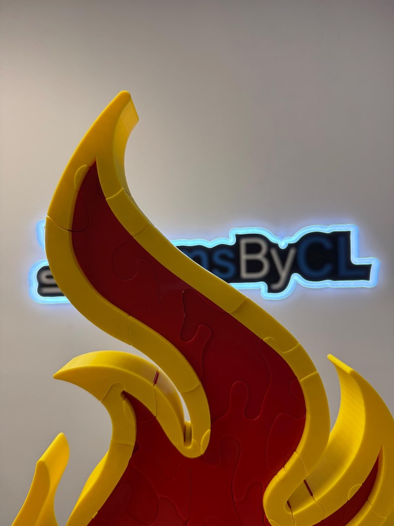 May include: A close-up of a flame-shaped puzzle. The puzzle is primarily red with yellow edges. The puzzle pieces are interlocking. The background has the text "Signs By CL" in a neon blue glow.