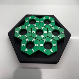 May include: A green and black hexagonal puzzle with a series of interlocking rings. Each ring has a number from 1 to 9 printed on it.