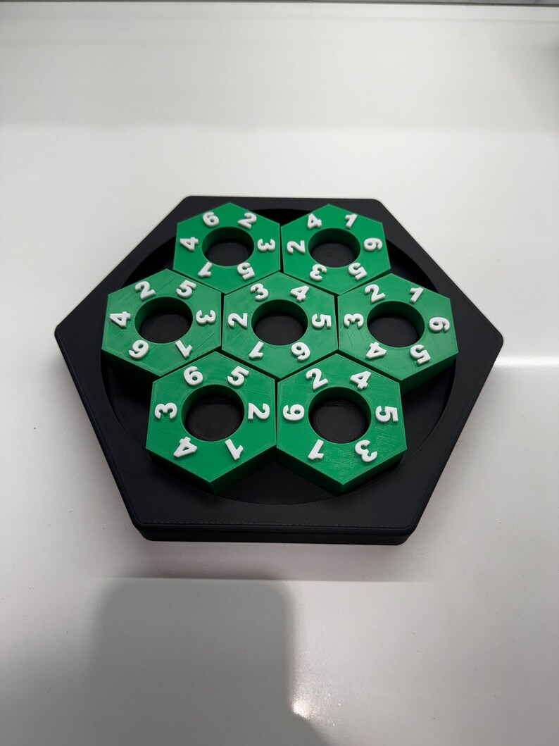 May include: A green and black hexagonal puzzle with a series of interlocking rings. Each ring has a number from 1 to 9 printed on it.