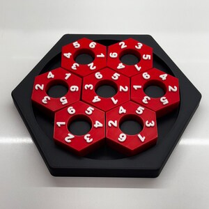 May include: A red hexagonal puzzle with white numbers on each piece. The puzzle is made up of six pieces that fit together to form a larger hexagon.