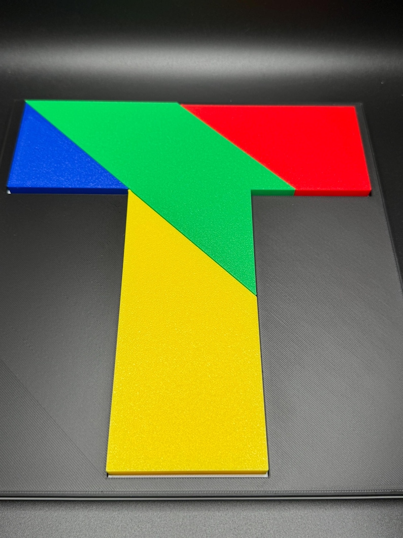 May include: A colorful wooden puzzle shaped like the letter T. The puzzle is made up of five pieces: a blue triangle, a green triangle, a red triangle, a yellow triangle, and a yellow square.