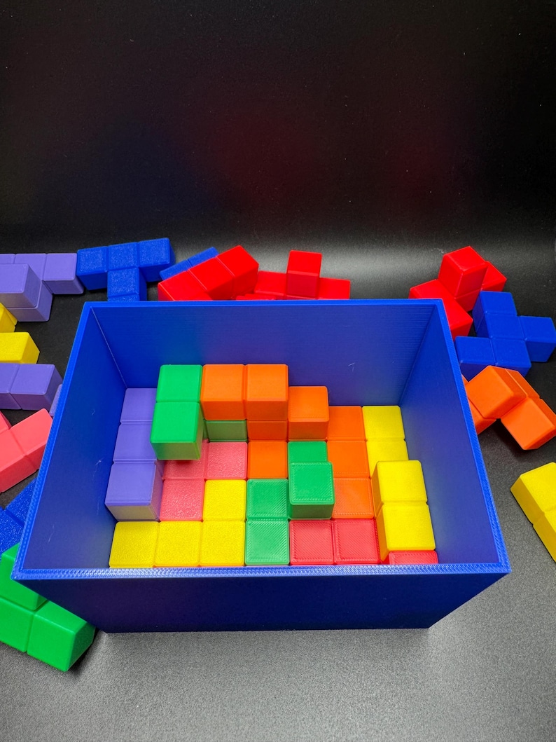 May include: A blue rectangular container filled with colorful, geometric building blocks. The blocks are various shapes and colors, including red, green, orange, yellow, and purple. Some blocks are outside the container.
