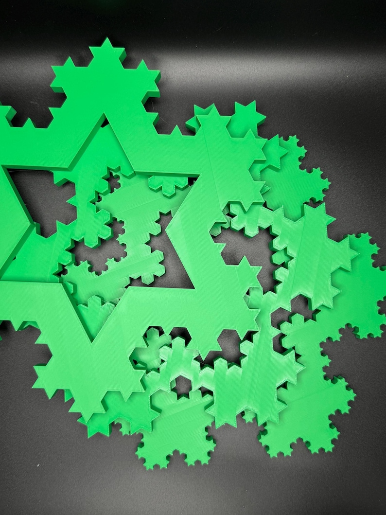 May include: A close-up of a green 3D printed fractal snowflake design. The snowflake is made up of many smaller snowflakes, creating a complex and intricate pattern.