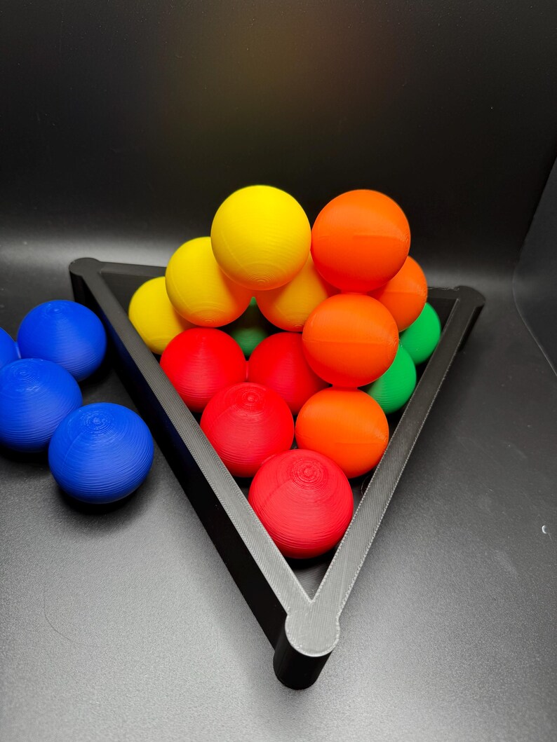 Peut inclure: Un support triangulaire noir contient une pyramide de boules color&eacute;es. Les boules sont rouges, orange, jaunes, vertes et bleues. Le support est sur une surface noire.