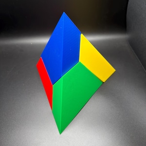 May include: A geometric pyramid puzzle toy composed of four distinct triangular faces in solid primary colors. The structure features a large blue face, a yellow face, a green face, and a red face, all meeting at a single top apex point.