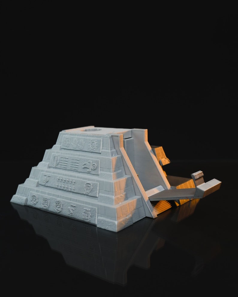 May include: A white 3D printed model of a Mayan pyramid with a ramp leading up to the top. The pyramid is decorated with intricate carvings and symbols.