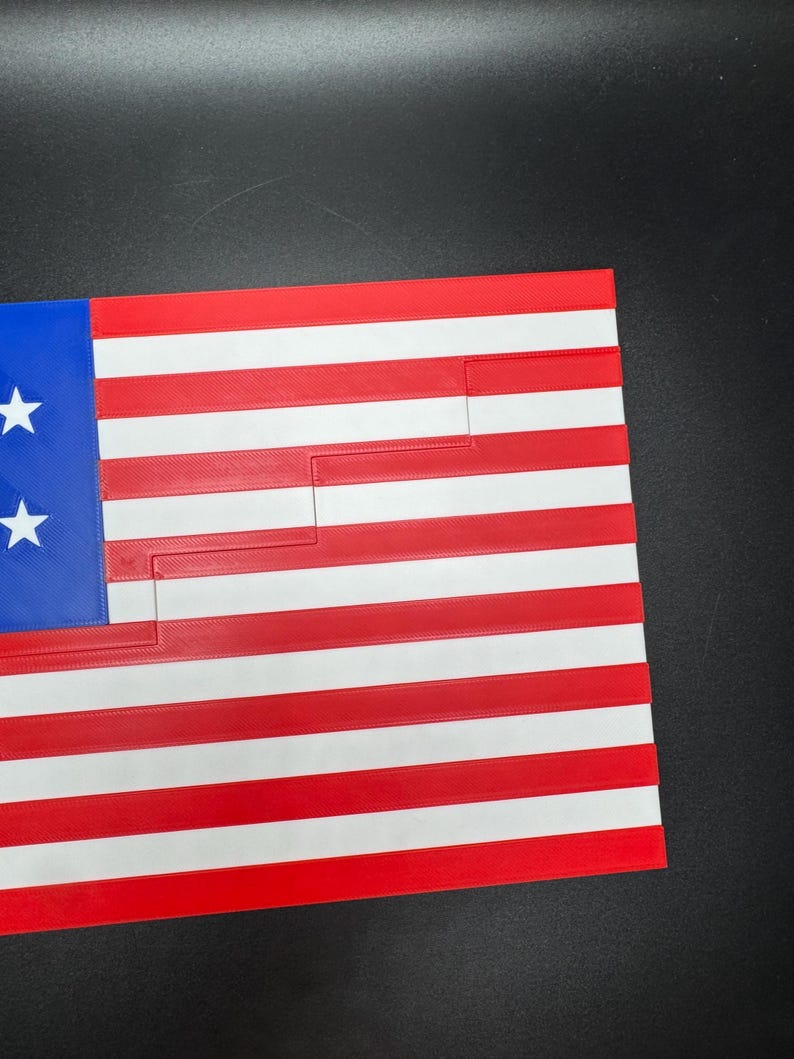 Puede incluir: Una bandera estadounidense roja, blanca y azul hecha de pl&aacute;stico. La bandera est&aacute; recortada de forma que crea un patr&oacute;n de escalera.