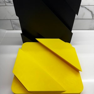 May include: Two geometric shapes, one black and one yellow, with a zig-zag pattern. The shapes are made of a smooth, hard material and appear to be 3D printed.