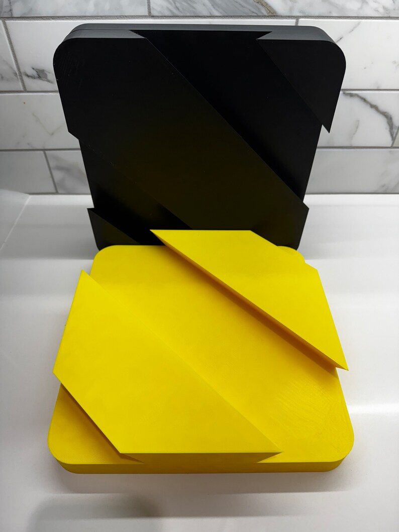 May include: Two geometric shapes, one black and one yellow, with a zig-zag pattern. The shapes are made of a smooth, hard material and appear to be 3D printed.