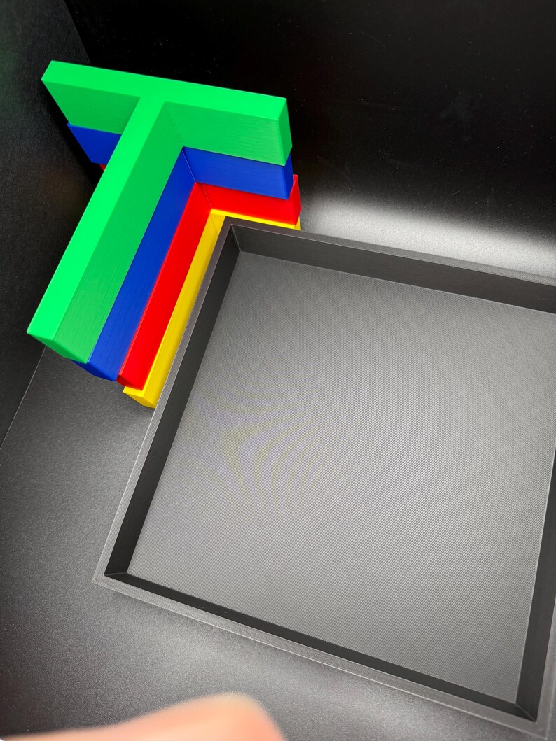 May include: A set of four colorful plastic corner protectors in green, blue, red, and yellow. The protectors are stacked on top of each other and are in the shape of a T. The protectors are in a black box.