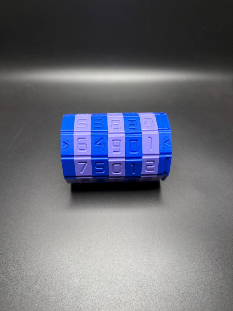 May include: A blue and purple combination lock toy with numbers. The toy is cylindrical with a checkerboard pattern of blue and purple squares. Numbers are printed on the purple squares. The background is a dark gray.