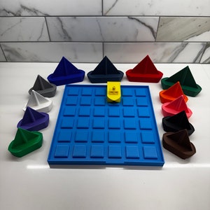 May include: A blue game board with 36 squares and 12 colorful toy sailboats. The sailboats are in various colors, including red, blue, green, white, black, and brown. A yellow toy boat is in the center of the board.