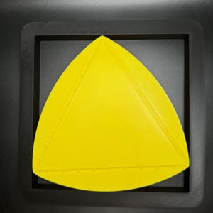 K&ouml;nnte beinhalten: Ein leuchtend gelbes, dreieckiges Objekt mit einer strukturierten Oberfl&auml;che, in Schwarz gerahmt.