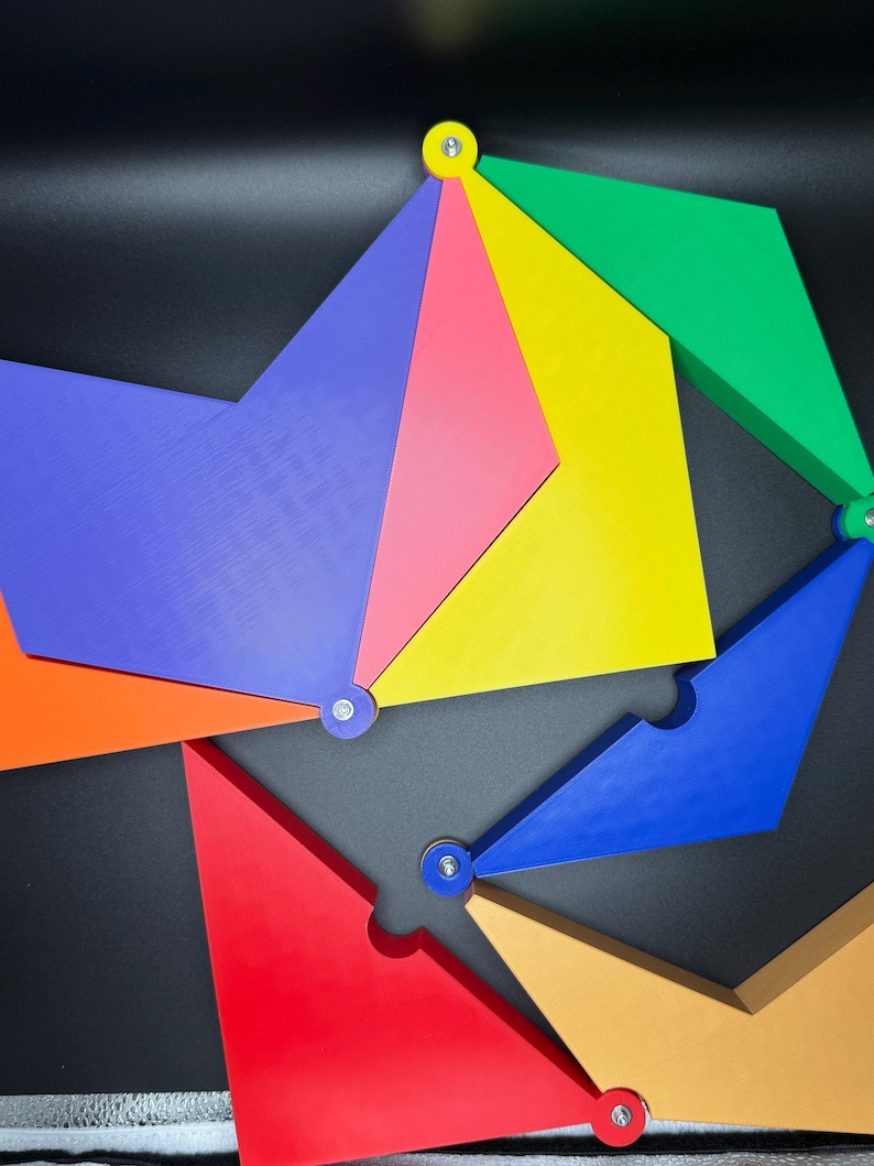 Peut inclure: Un puzzle g&eacute;om&eacute;trique color&eacute; compos&eacute; de diverses formes et couleurs, notamment le rouge, le bleu, le jaune, le vert et l'orange. Les pi&egrave;ces sont reli&eacute;es par de petites attaches m&eacute;talliques, cr&eacute;ant un design visuellement attrayant. Le puzzle est pos&eacute; sur un fond sombre.