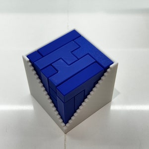 Puede incluir: Un rompecabezas 3D azul en forma de cubo, ensamblado y colocado en un marco blanco. El rompecabezas est&aacute; hecho de piezas que se entrelazan para formar un patr&oacute;n geom&eacute;trico.