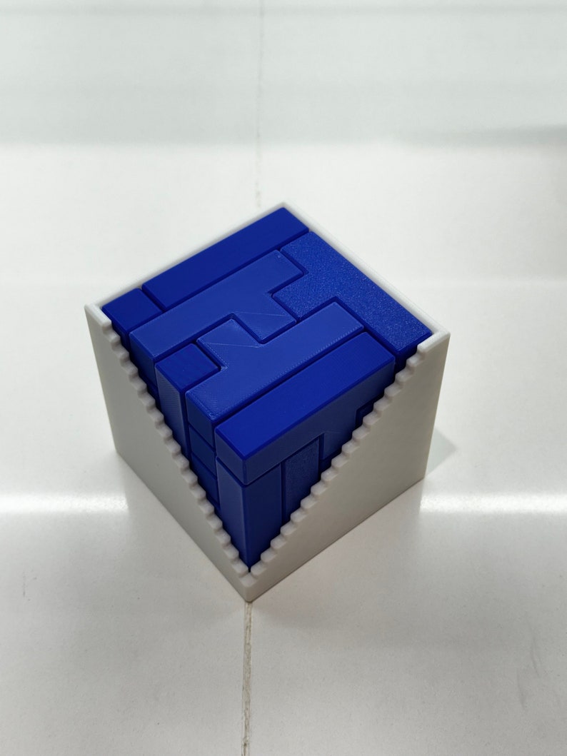 Puede incluir: Un rompecabezas 3D azul en forma de cubo, ensamblado y colocado en un marco blanco. El rompecabezas est&aacute; hecho de piezas que se entrelazan para formar un patr&oacute;n geom&eacute;trico.