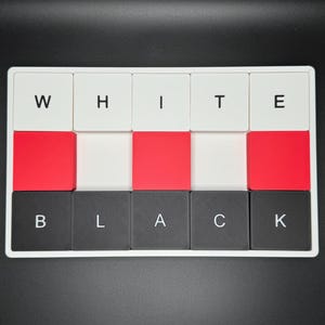 May include: A rectangular puzzle with the words "WHITE" and "BLACK" spelled out using individual letter blocks. The blocks are white, red, and black, arranged in a grid pattern. The puzzle is set against a black background.