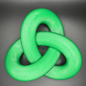 May include: A green plastic three-dimensional knot, also known as a triquetra, is a decorative object. The knot is made of three interlocked loops.