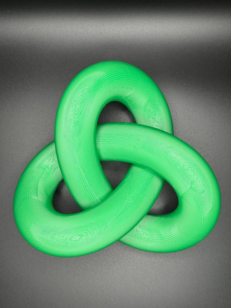 May include: A green plastic three-dimensional knot, also known as a triquetra, is a decorative object. The knot is made of three interlocked loops.