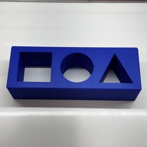 May include: A blue plastic block with cutouts of a square, circle, and triangle.