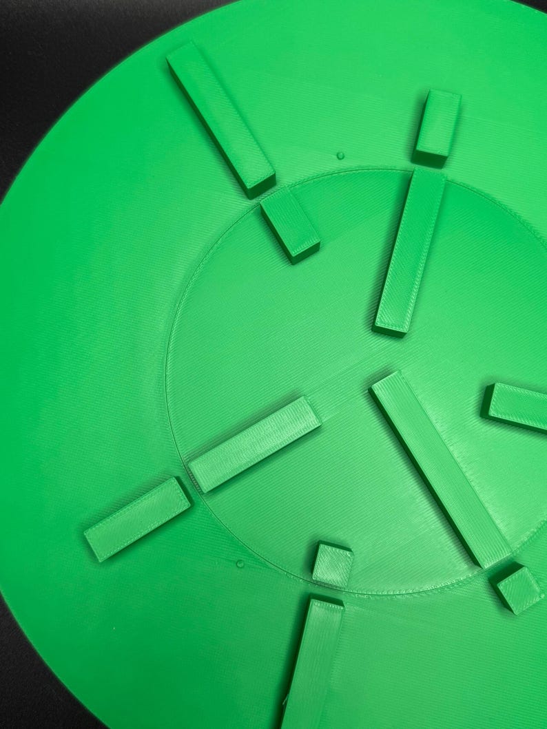 May include: Bright green, circular object with a series of rectangular and square protrusions. The object has a textured surface and a central circular indentation. The design suggests a functional or decorative item.