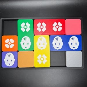 May include: A set of colorful square tiles with different images, including flowers and faces. The tiles are arranged in a grid pattern on a black surface.