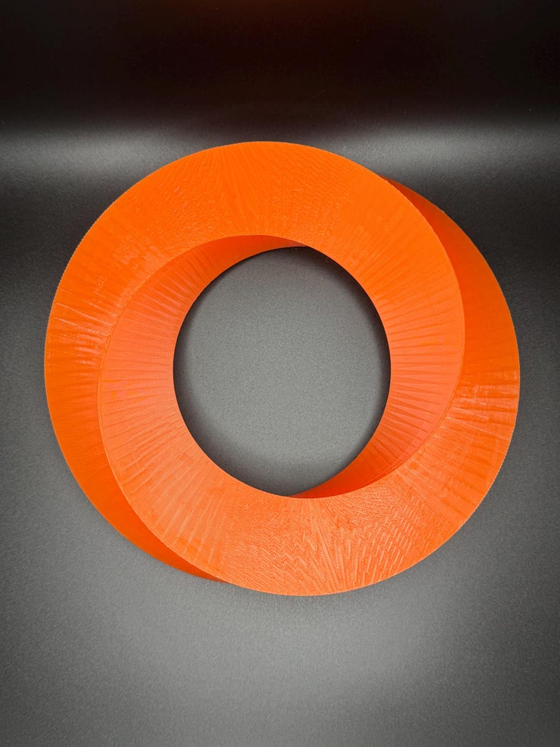 May include: A bright orange, 3D printed, Mobius strip sculpture. The sculpture is shaped like a ring with a twist in the middle.