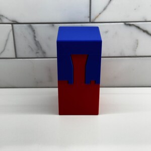 May include: A red and blue box with a unique design. The top of the box is blue and the bottom is red. The box has a cutout in the middle.