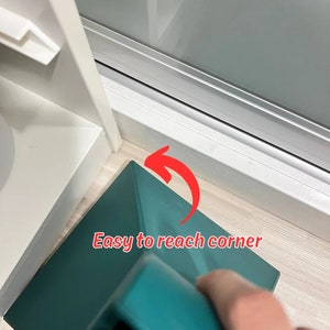 May include: A teal-colored cleaning tool with a triangular head, designed to reach hard-to-clean corners. The tool is positioned in a corner, with a red arrow pointing to the corner and the text "Easy to reach corner".