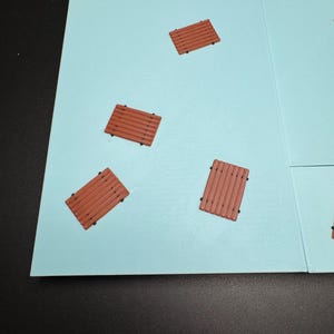 May include: A light blue game board with several small, brown, wooden-looking platforms scattered across its surface. The platforms have a rectangular shape with parallel lines and small black dots.