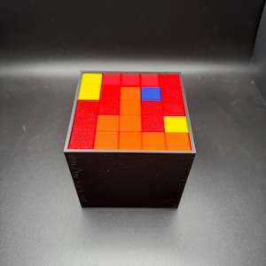 May include: A black cube with a red, orange, yellow, and blue mosaic pattern on the top.