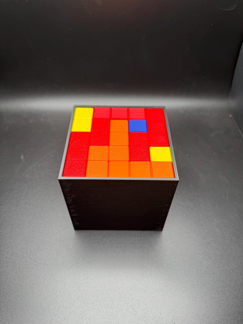 May include: A black cube with a red, orange, yellow, and blue mosaic pattern on the top.