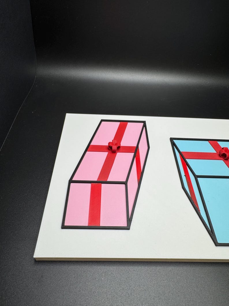 May include: Two 3D-printed gift boxes on a white surface. One is pink with red ribbon and a bow, the other is blue with red ribbon and a bow. Both have black outlines.