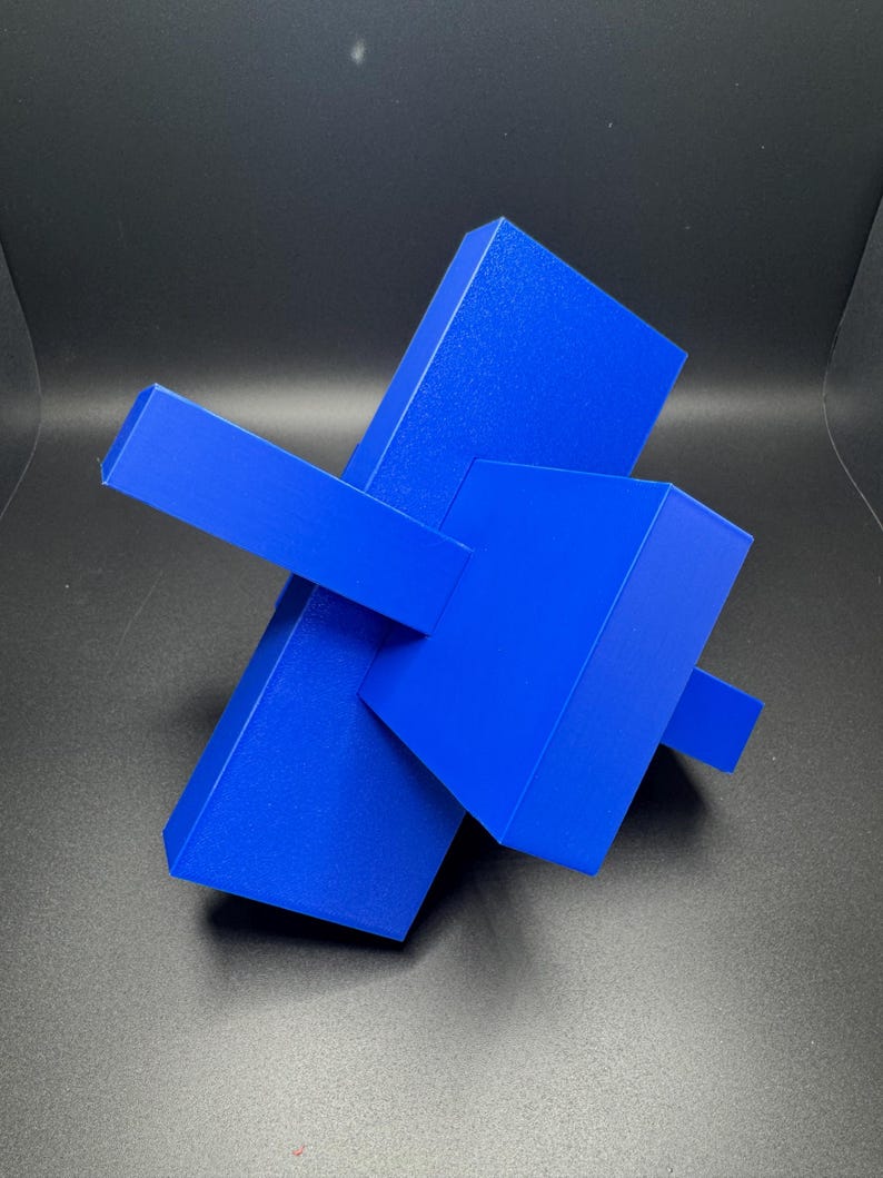 K&ouml;nnte beinhalten: Eine blaue abstrakte Skulptur aus geometrischen Formen. Die Skulptur besteht aus drei rechteckigen Prismen, die &uuml;bereinander gestapelt sind und sich in verschiedenen Winkeln schneiden.