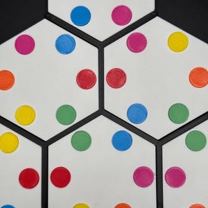 May include: A white hexagonal board with black lines dividing it into sections. Each section has colorful circles in various colors, including red, yellow, blue, green, and orange.