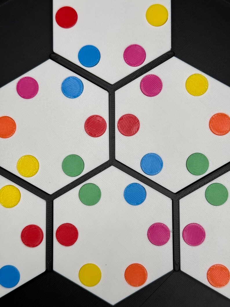 May include: A white hexagonal board with black lines dividing it into sections. Each section has colorful circles in various colors, including red, yellow, blue, green, and orange.