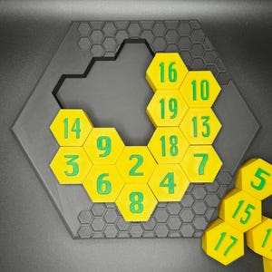 Puede incluir: Un juego de rompecabezas hexagonal con fichas hexagonales amarillas numeradas del 1 al 19. Las fichas est&aacute;n dispuestas en un patr&oacute;n de panal, con algunas fichas que faltan. El rompecabezas est&aacute; hecho de pl&aacute;stico negro.