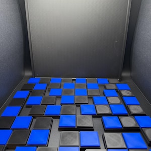 May include: A display of black and blue square tiles arranged in a grid pattern. The tiles are set against a dark background, creating a contrast between the colors. The arrangement suggests a puzzle or a design element.