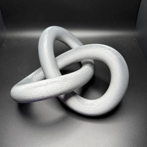 May include: A gray, three-dimensional, abstract sculpture made of smooth, rounded, interconnected loops.