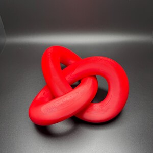 May include: A red, three-dimensional knot sculpture. The knot is made of smooth, rounded plastic and is tied in a complex pattern.