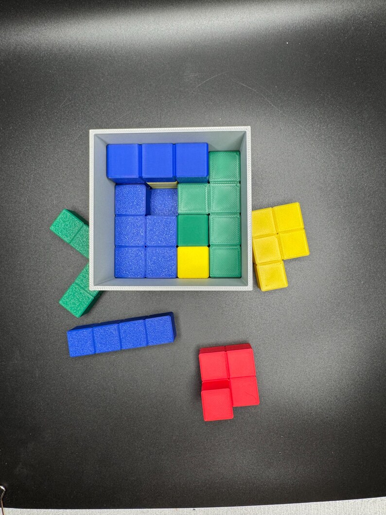 Puede incluir: Un conjunto de bloques de madera de colores en varias formas y tama&ntilde;os. Los bloques est&aacute;n dispuestos en una caja cuadrada, con algunos bloques fuera de la caja. Los bloques son azules, verdes, amarillos y rojos.