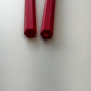 May include: Two red hexagonal pencils with a triangular and square shaped end.