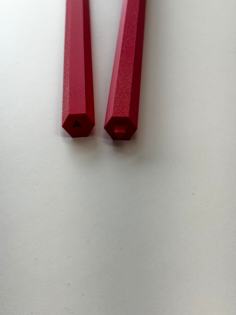 May include: Two red hexagonal pencils with a triangular and square shaped end.