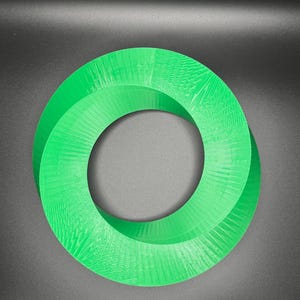 May include: A green 3D printed Mobius strip, a continuous loop with a twist, against a dark gray background.