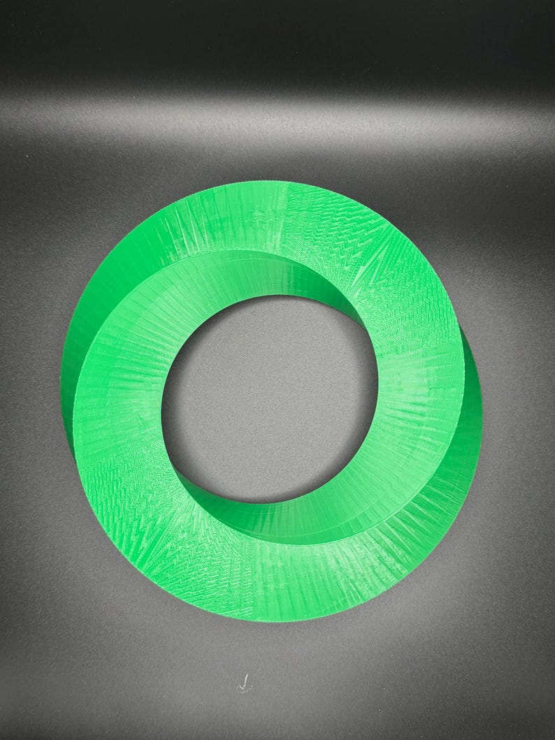 May include: A green 3D printed Mobius strip, a continuous loop with a twist, against a dark gray background.