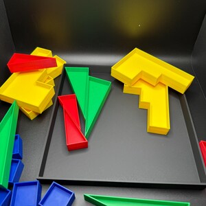 May include: A set of colorful plastic geometric shapes, including squares, triangles, and rectangles, in red, yellow, green, and blue. The shapes are arranged on a black tray.