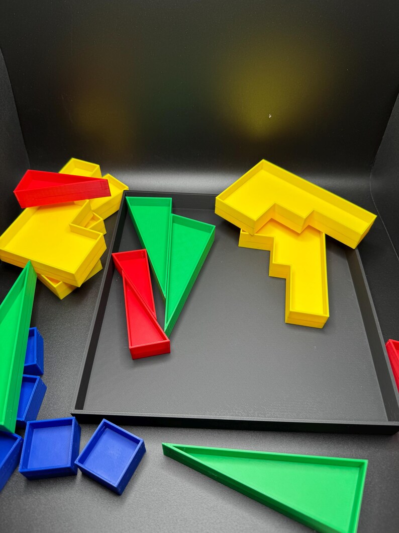 May include: A set of colorful plastic geometric shapes, including squares, triangles, and rectangles, in red, yellow, green, and blue. The shapes are arranged on a black tray.