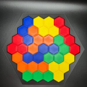May include: A hexagonal puzzle with a spiral pattern made of colorful plastic tiles. The tiles are red, orange, yellow, green, and blue.